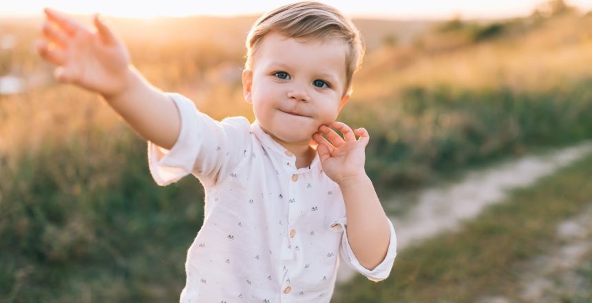 adorable little child smiling at camera while walking outdoors at sunset